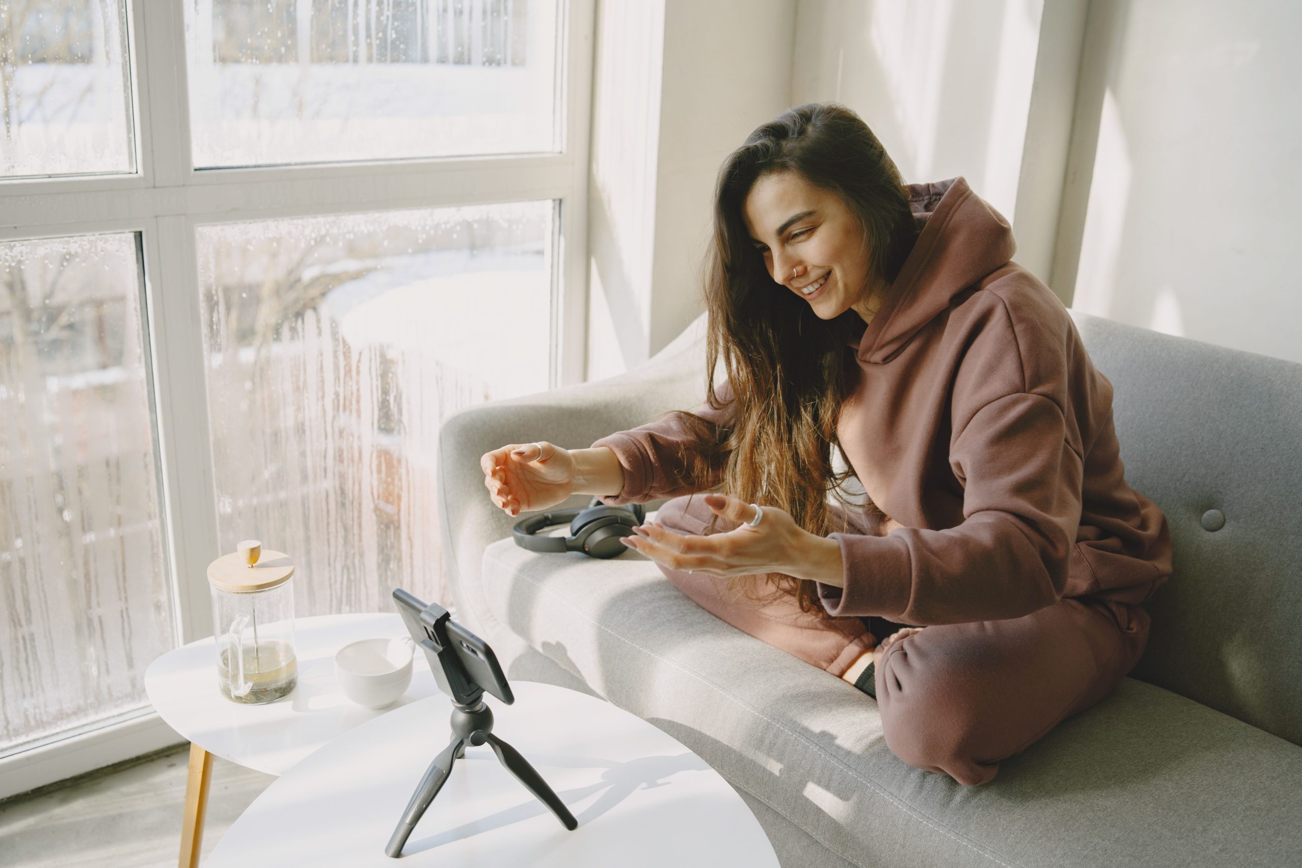 A woman records a casual video at home with a smartphone and tripod, illustrating creator-led digital companionship.