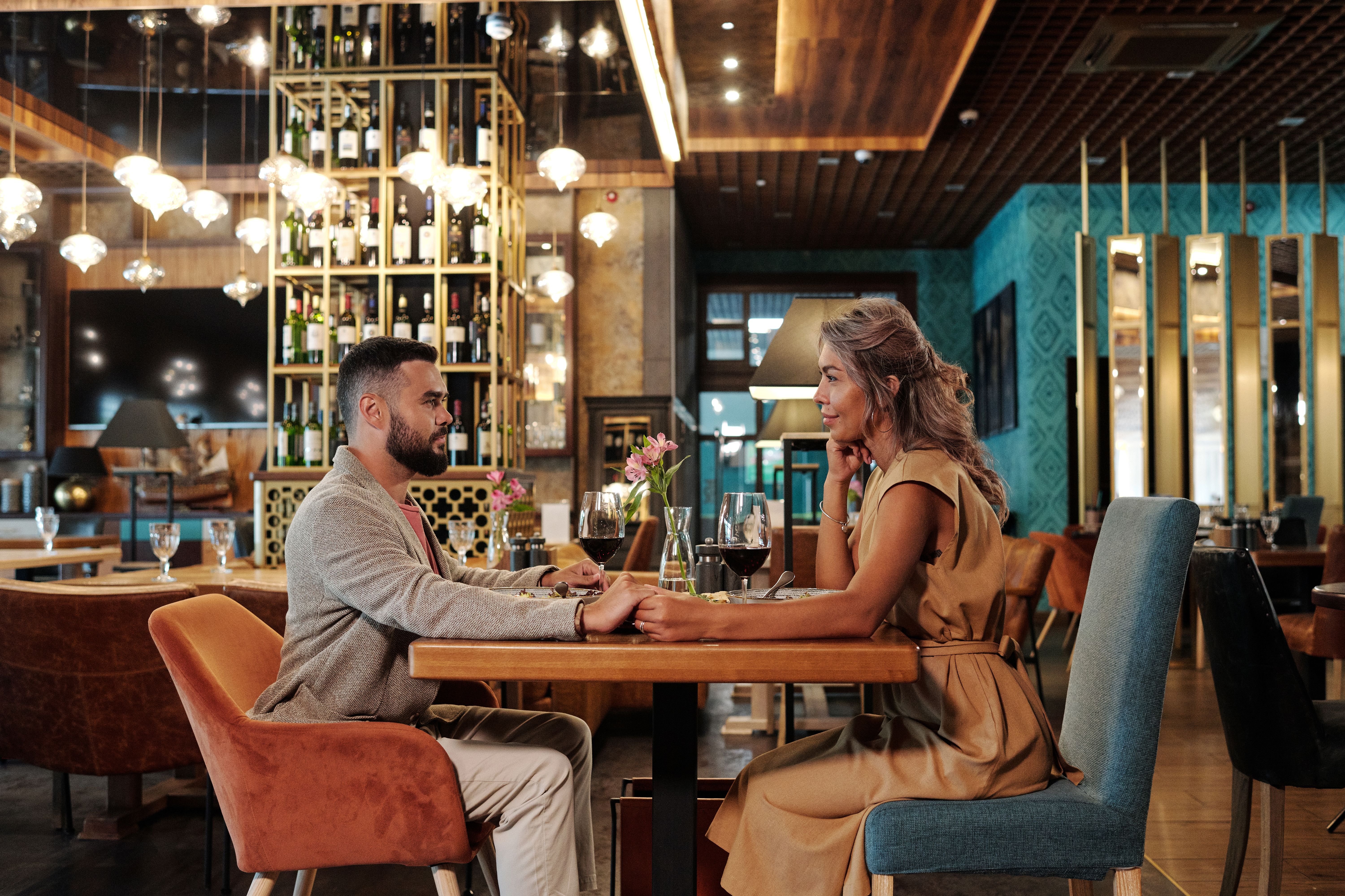 A couple enjoys an intimate dinner in an elegant restaurant, illustrating the in-person date experience offered as companionship.
